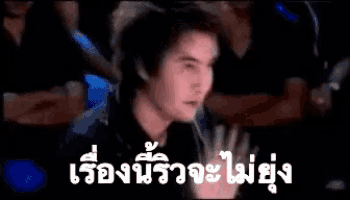 a man is sitting in a dark room with a crowd behind him and a foreign language written on the screen .