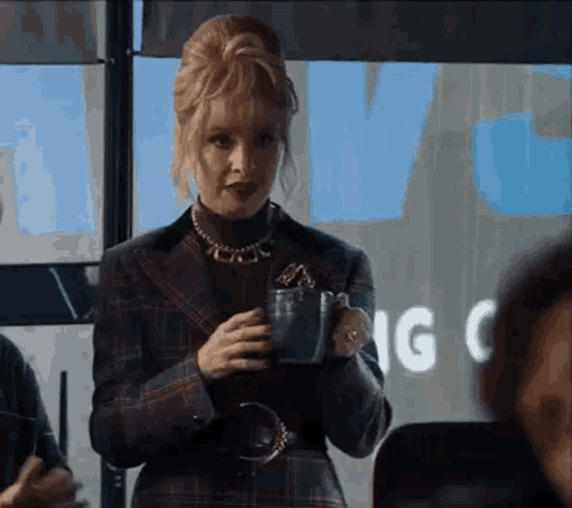 a woman in a plaid jacket is holding a cup of coffee in her hand .