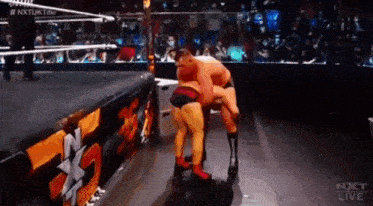 two men are wrestling in a wrestling ring with the words nxt live on the bottom of the screen .