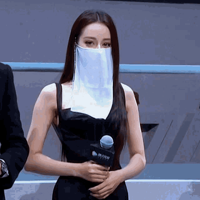 a woman wearing a mask is holding a microphone and a sign that says ' a ' on it