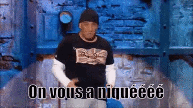 a man in a black shirt is standing in front of a brick wall and says on vous a niqueeee .