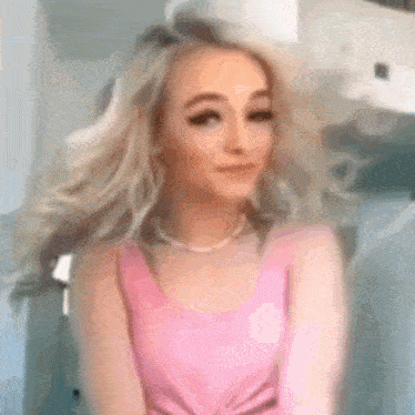 a woman in a pink tank top and a pearl necklace is looking at the camera .