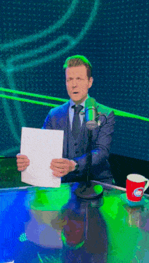 a man in a suit and tie is standing in front of a microphone holding a piece of paper