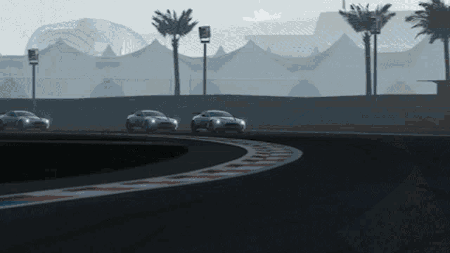 a group of cars are driving on a race track with palm trees in the background