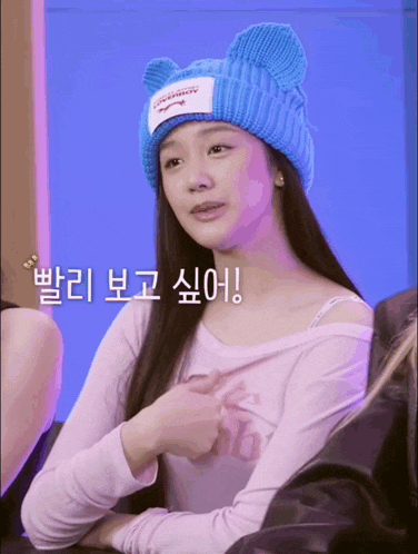 a woman wearing a blue hat with ears is sitting in front of a purple background