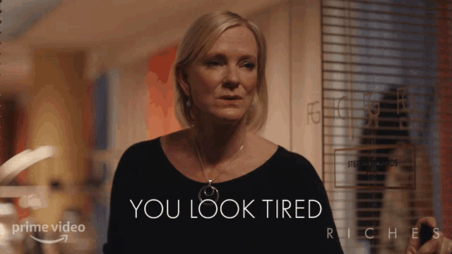 a woman is standing in front of a sign that says " you look tired "