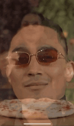 a man wearing sunglasses looks at a pizza on a table .