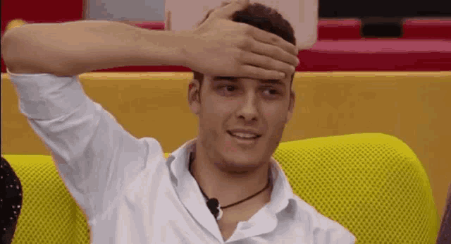 a man covering his face with his hand while sitting on a yellow couch .
