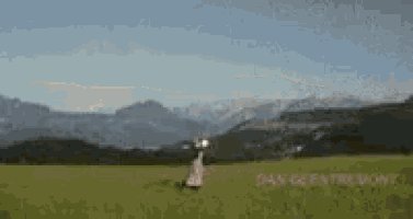 a woman in a white dress is standing in a grassy field with mountains in the background .
