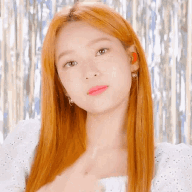 a close up of a woman with long red hair wearing earrings and a white dress .