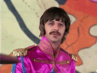 a man in a pink uniform with a mustache is sitting in front of a wall .