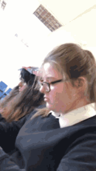 a girl wearing glasses sits in a classroom with other girls
