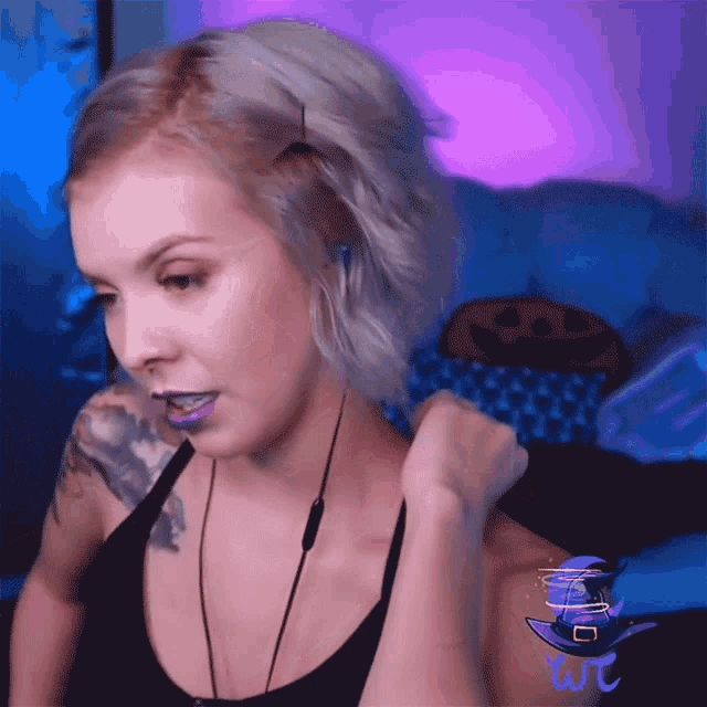a woman wearing purple lipstick and a black tank top has a witch hat on her arm