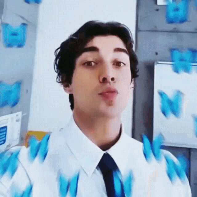 a man in a white shirt and tie is blowing a kiss with blue butterflies behind him