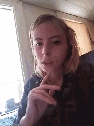 a girl is taking a selfie in front of a window with her hand on her chin