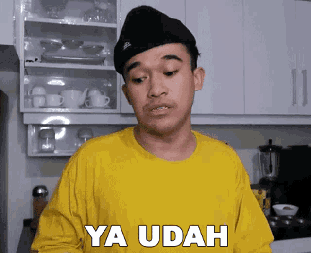 a young man wearing a yellow shirt and a black hat says ya udah