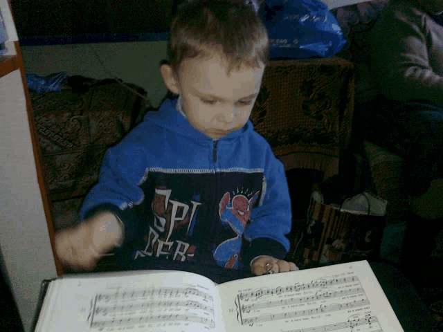 a young boy wearing a spider-man jacket is reading a book of music