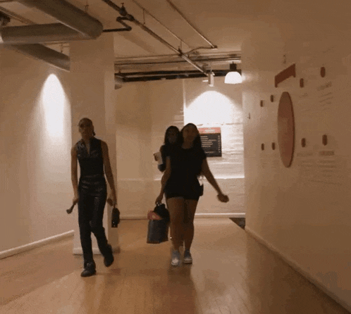 two women are walking down a hallway with a sign on the wall that says ' a '