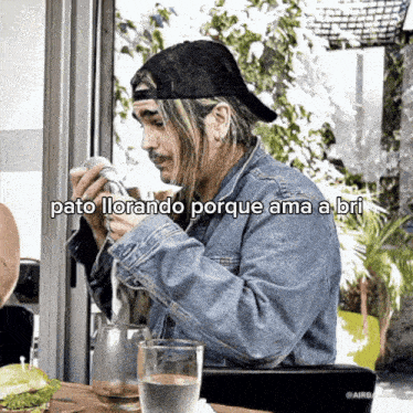 a man in a denim jacket is sitting at a table with a glass of water and a sandwich ..