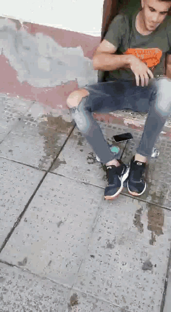 a man is smoking a cigarette while sitting on a sidewalk .