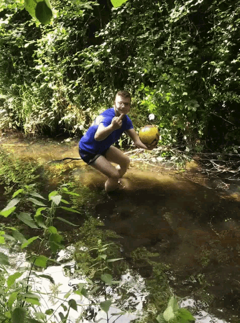 a man kneeling in a stream holding a yellow ball