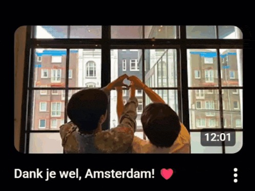 two people are making a heart shape with their hands in front of a window with the time 12:01