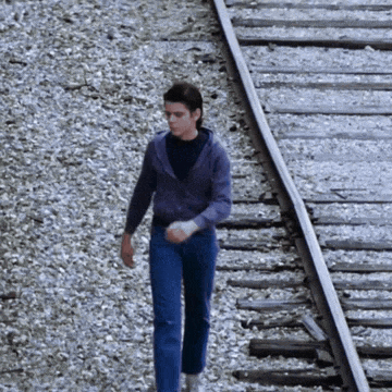 a man in a purple sweater and blue jeans is walking on train tracks