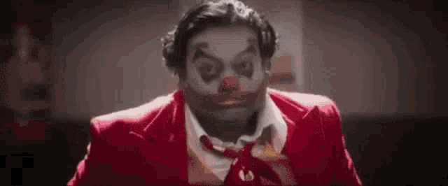 a man in a red suit and tie is dressed as a clown and making a funny face .