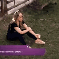 a woman is sitting on the grass with a purple sign in the background .