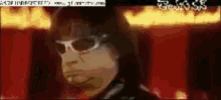 a man wearing sunglasses stands in front of a fire