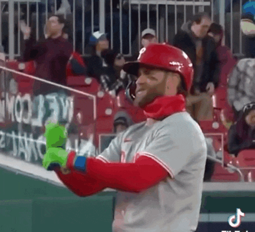 a baseball player wearing a red helmet and green gloves is standing on the field .
