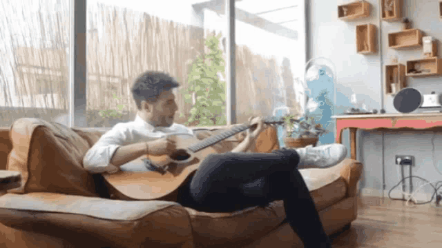 a man is sitting on a couch playing an acoustic guitar