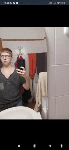a man taking a selfie in a bathroom with the time of 12:49 on his phone