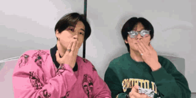 a man in a pink jacket and a man in a green sweatshirt are covering their mouths with their hands