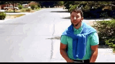 a man wearing a blue sweater and a green shirt is standing on a sidewalk .