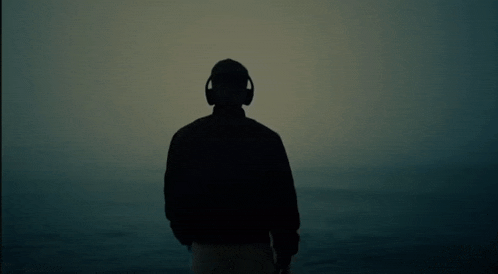 a silhouette of a man wearing headphones stands in front of a body of water