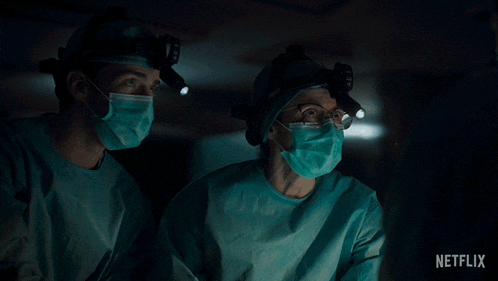 a man and a woman wearing surgical gowns and masks are looking at a screen with a netflix logo visible