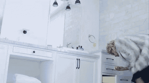 a woman in a fur coat is standing in a bathroom with white cabinets