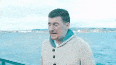 a man in a sweater is standing on a pier overlooking the water .