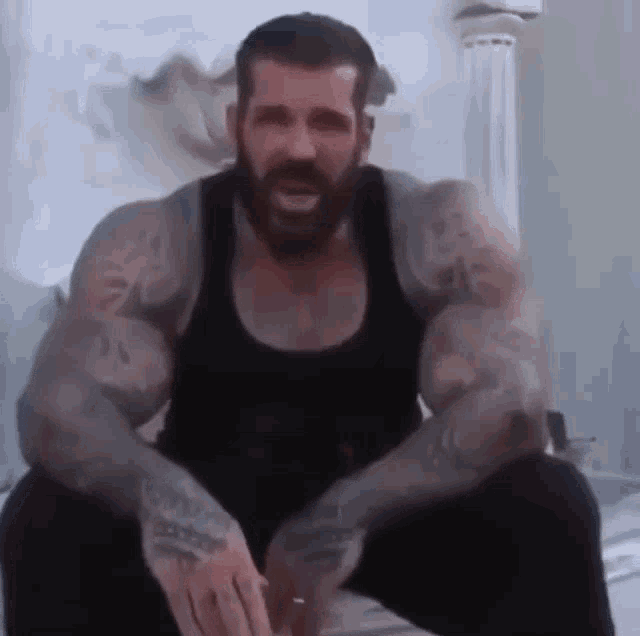 a man with a beard and tattoos on his arms is sitting down .