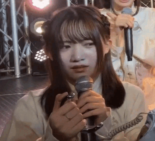 a girl is holding a microphone in front of her face while another girl holds a microphone in the background .