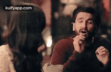 a man with a beard is singing into a microphone while sitting next to a woman .