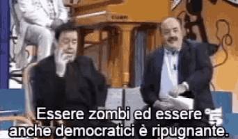 two men are sitting next to each other in front of a piano and a sign that says essere zombi ed essere