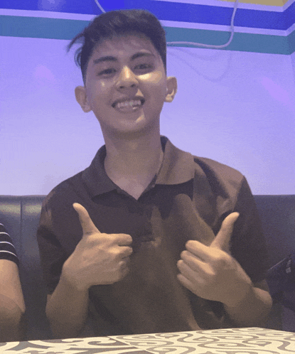 a young man giving a thumbs up while sitting on a couch