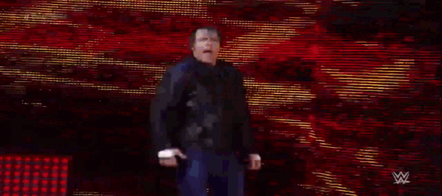 a man in a black jacket is walking on a stage in front of a red and yellow background .