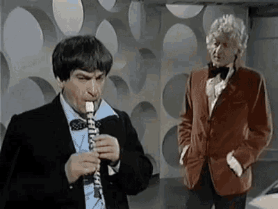 a man in a suit and bow tie is playing a clarinet while another man stands behind him .