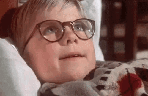 a young boy wearing glasses is laying in a bed with a blanket .