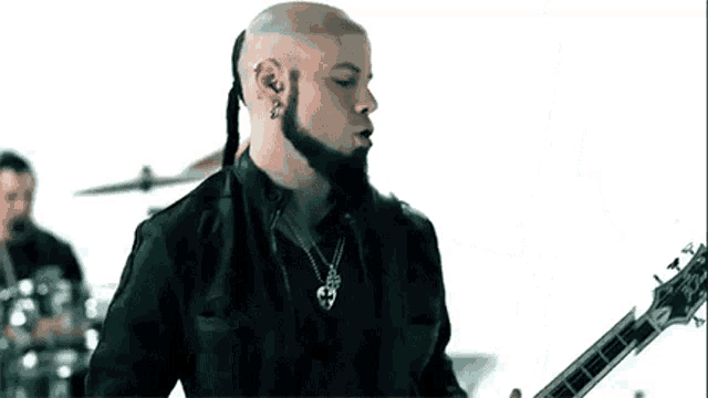 a bald man with a beard is playing a guitar in front of a drum set .
