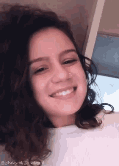 a woman with curly hair and a nose ring smiles for the camera .