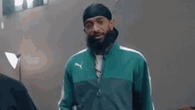 a man with a beard wearing a green jacket and a black headband is smiling .